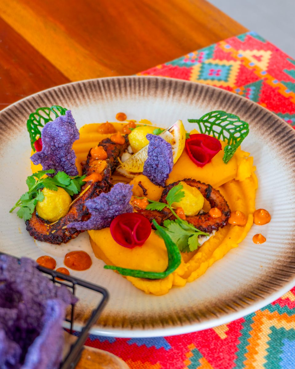 Grilled octopus plated with saffron purée, purple chips and herbs.