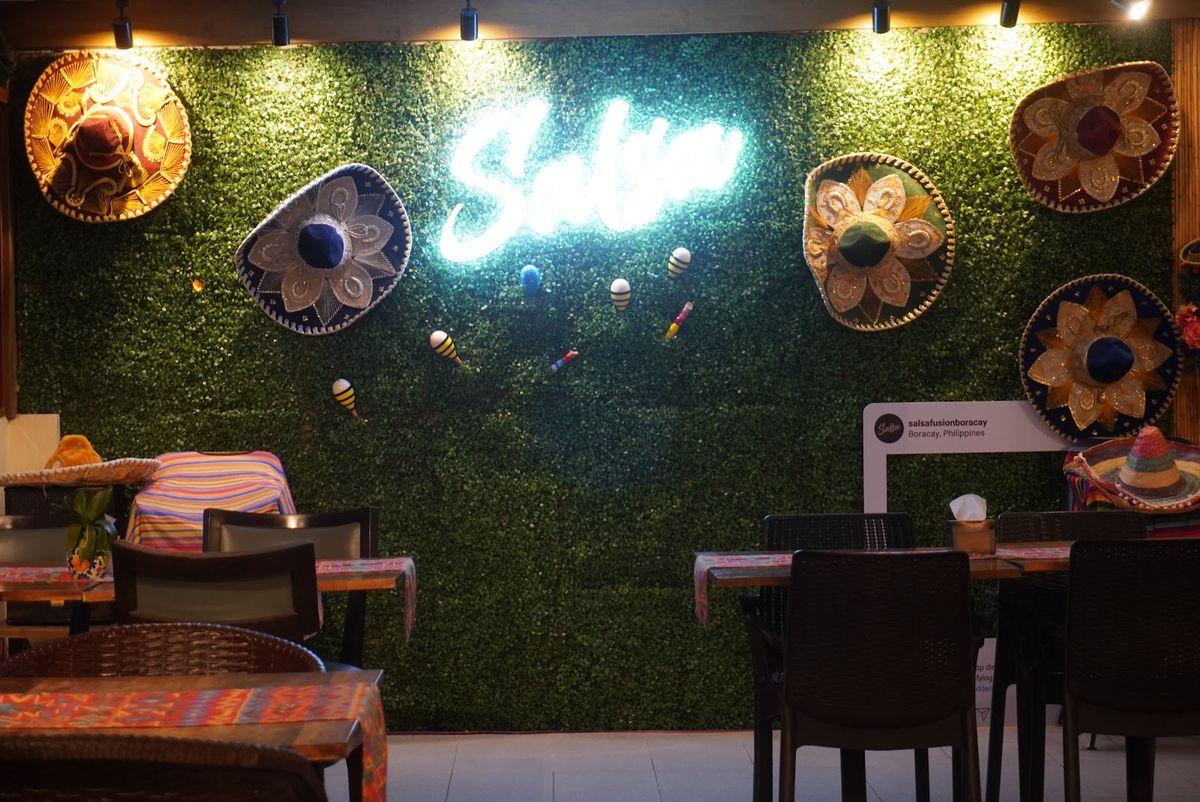 The glowing Salsa neon sign on a green wall decorated with sombreros.