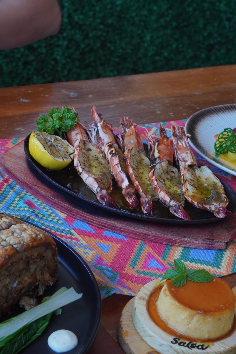 Grilled prawns with lemon beside a Salsa leche flan on a colourful woven runner.