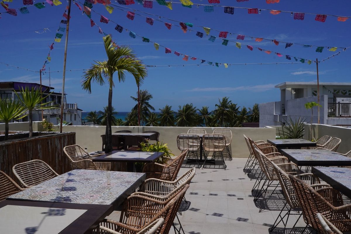 Salsa's rooftop terrace by day, rattan chairs under strings of papel picado bunting and palm trees.