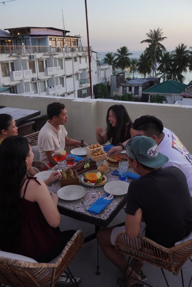 Friends sharing plates at a rooftop table in the golden-hour light, palm trees behind them.