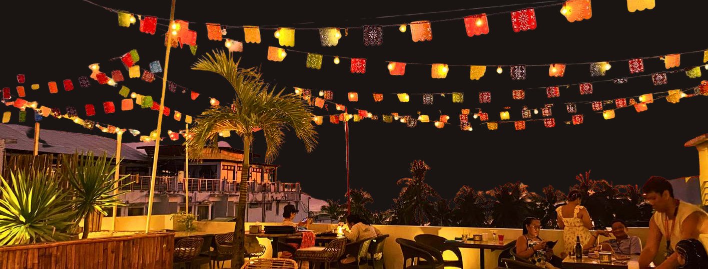 Salsa's rooftop terrace at night under strings of glowing papel picado lanterns and palm trees.