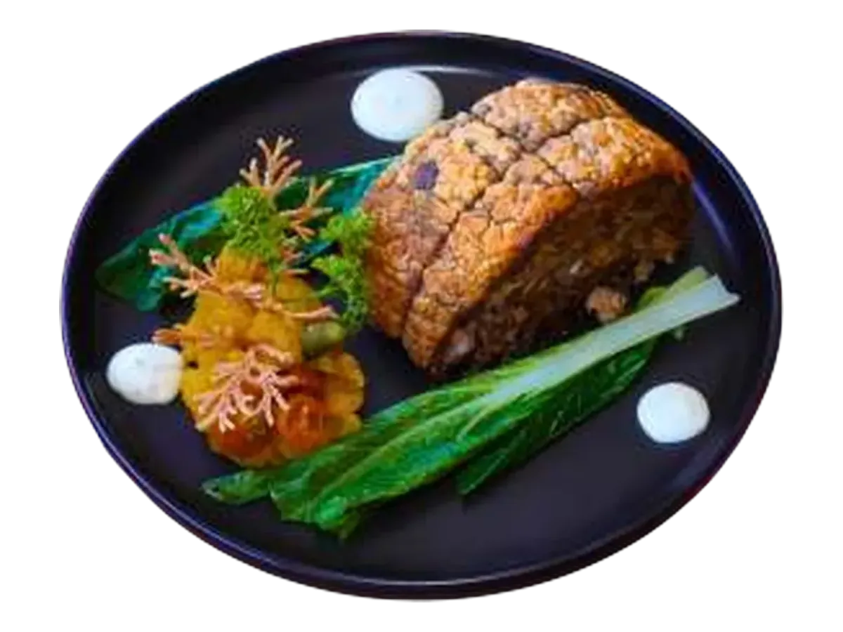 A slab of crispy-skinned pork belly with pickled vegetables and greens on a dark plate.
